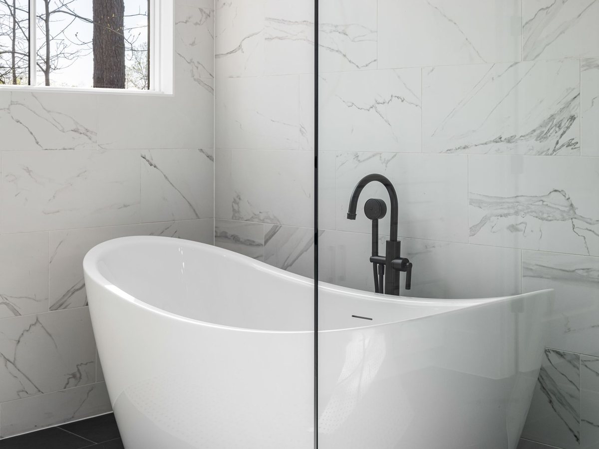 Baignoire îlot devant un mur en marbre avec robinetterie noire sur pied